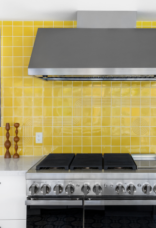 A JennAir® NOIR™ Professional Range and Commercial Hood in a kitchen with a yellow backsplash. A JennAir® NOIR™ Professional Range and Commercial Hood in a kitchen with a yellow backsplash.