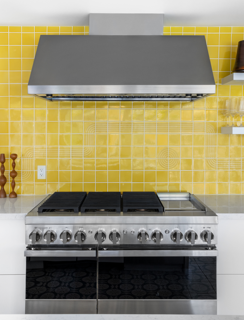 A JennAir® NOIR™ Professional Range and Commercial Hood in a kitchen with a yellow backsplash. A JennAir® NOIR™ Professional Range and Commercial Hood in a kitchen with a yellow backsplash.