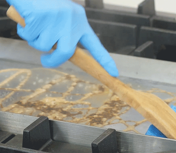 Closeup of a person wiping the griddle with a sponge.