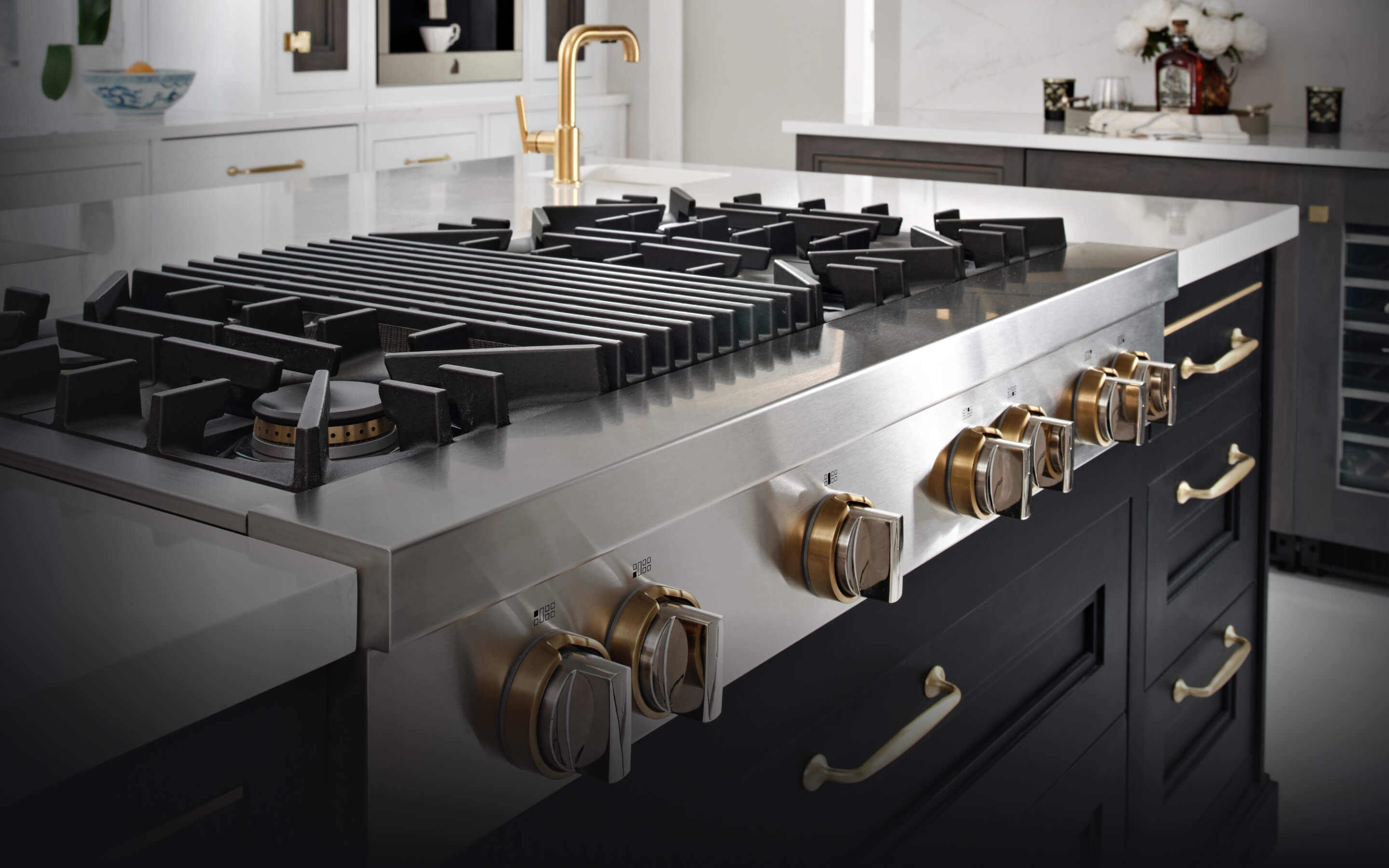 A JennAir® Gas Rangetop in a kitchen with dark cabinets and brass accents. A JennAir® Gas Rangetop in a kitchen with dark cabinets and brass accents.
