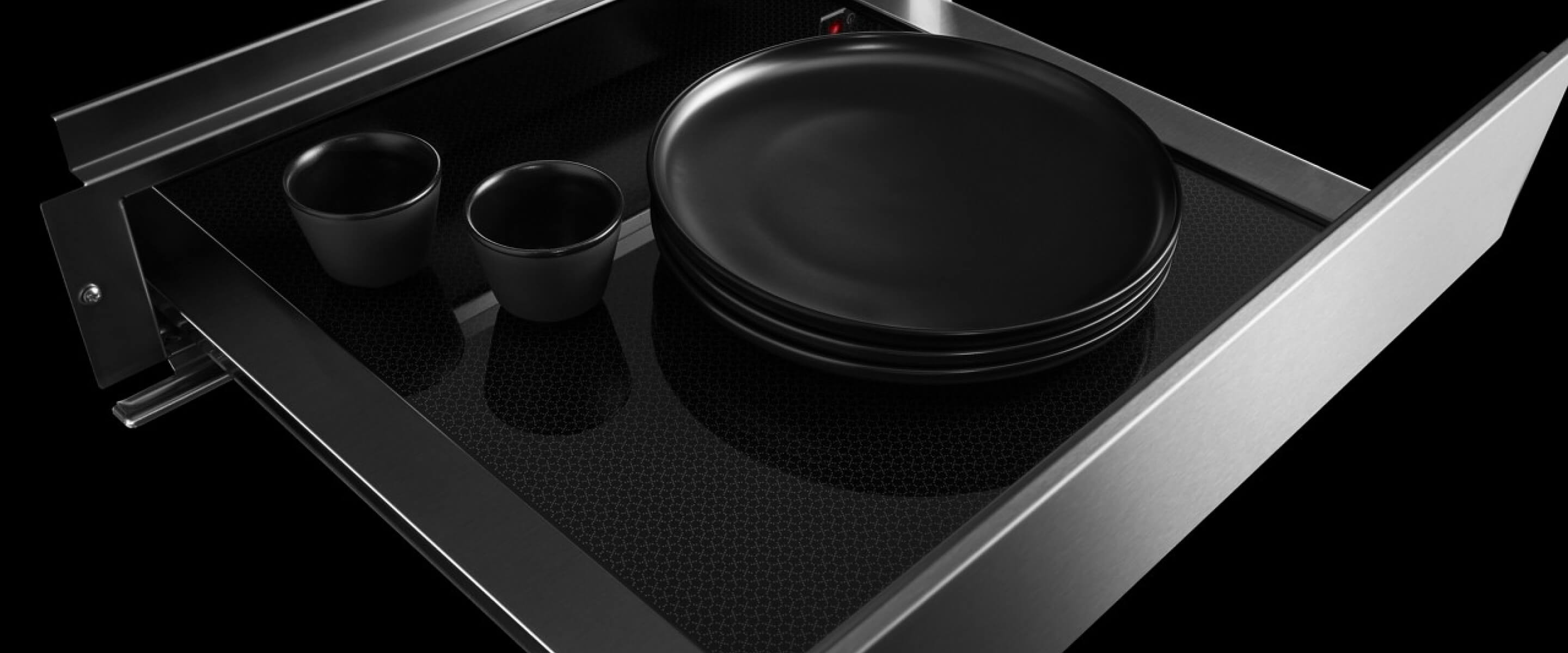 An open JennAir® 24-inch warming drawer with plates and mugs inside.