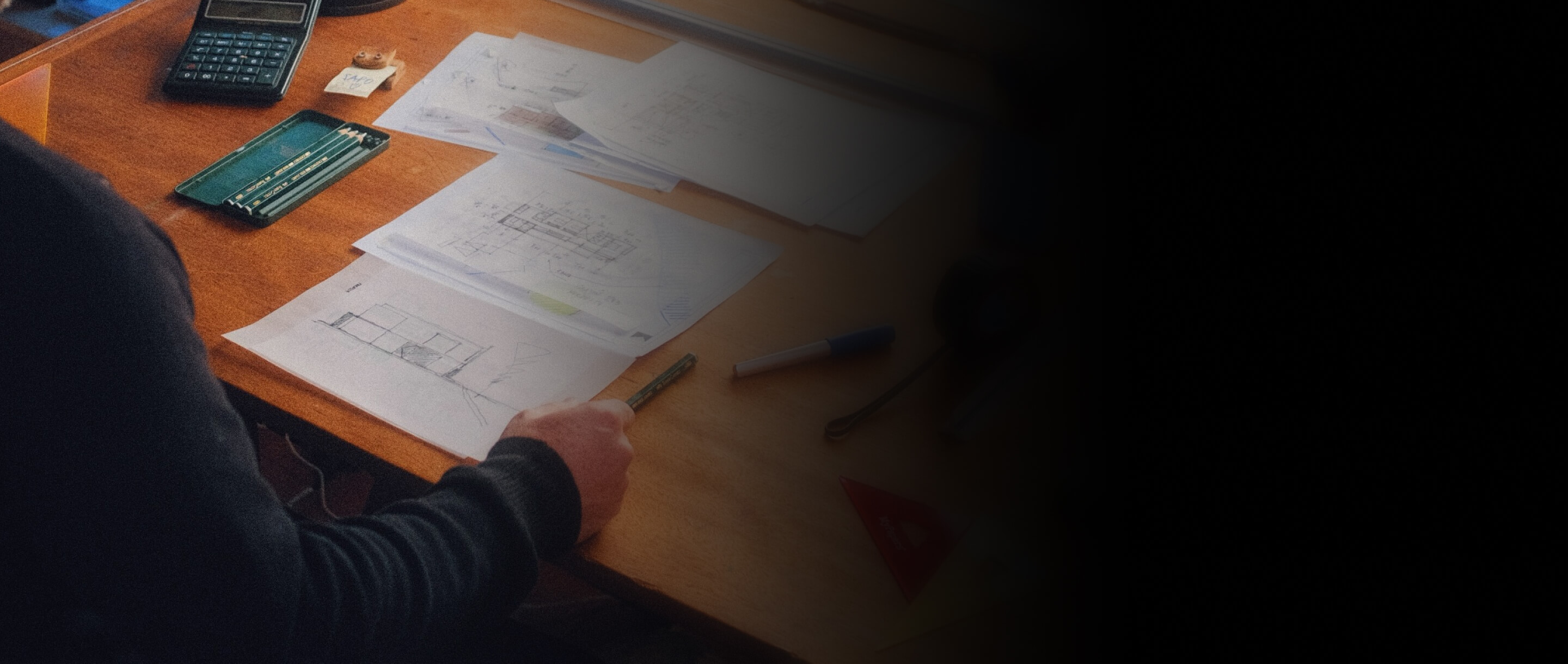 A person sitting at a workspace covered in architect's tools.
