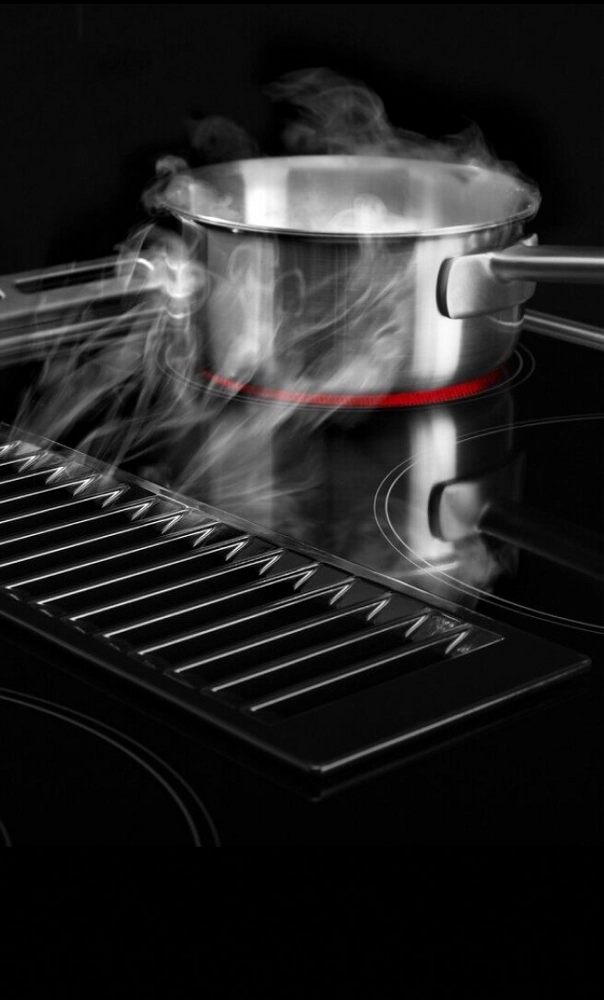 Steam being whisked away from a steel pot by downdraft ventilation.