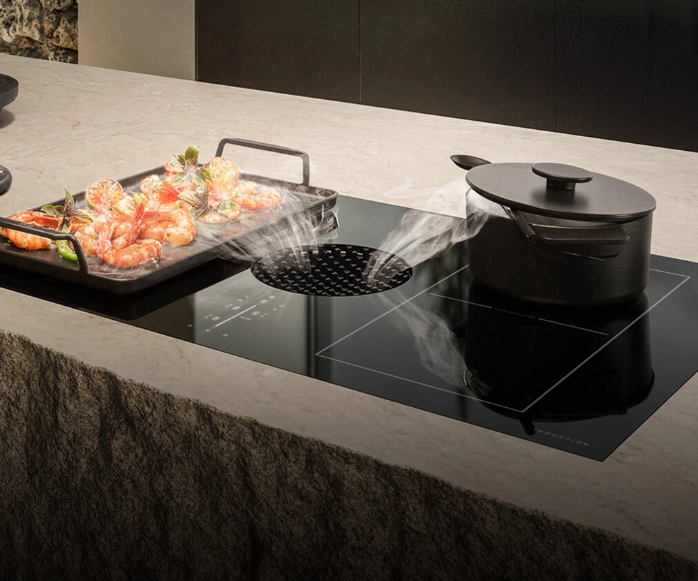 A griddle of shrimp cooking on a downdraft cooktop.