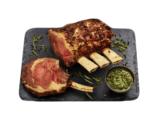 A cooked medium-rare crown roast on a slate with chimichurri sauce.